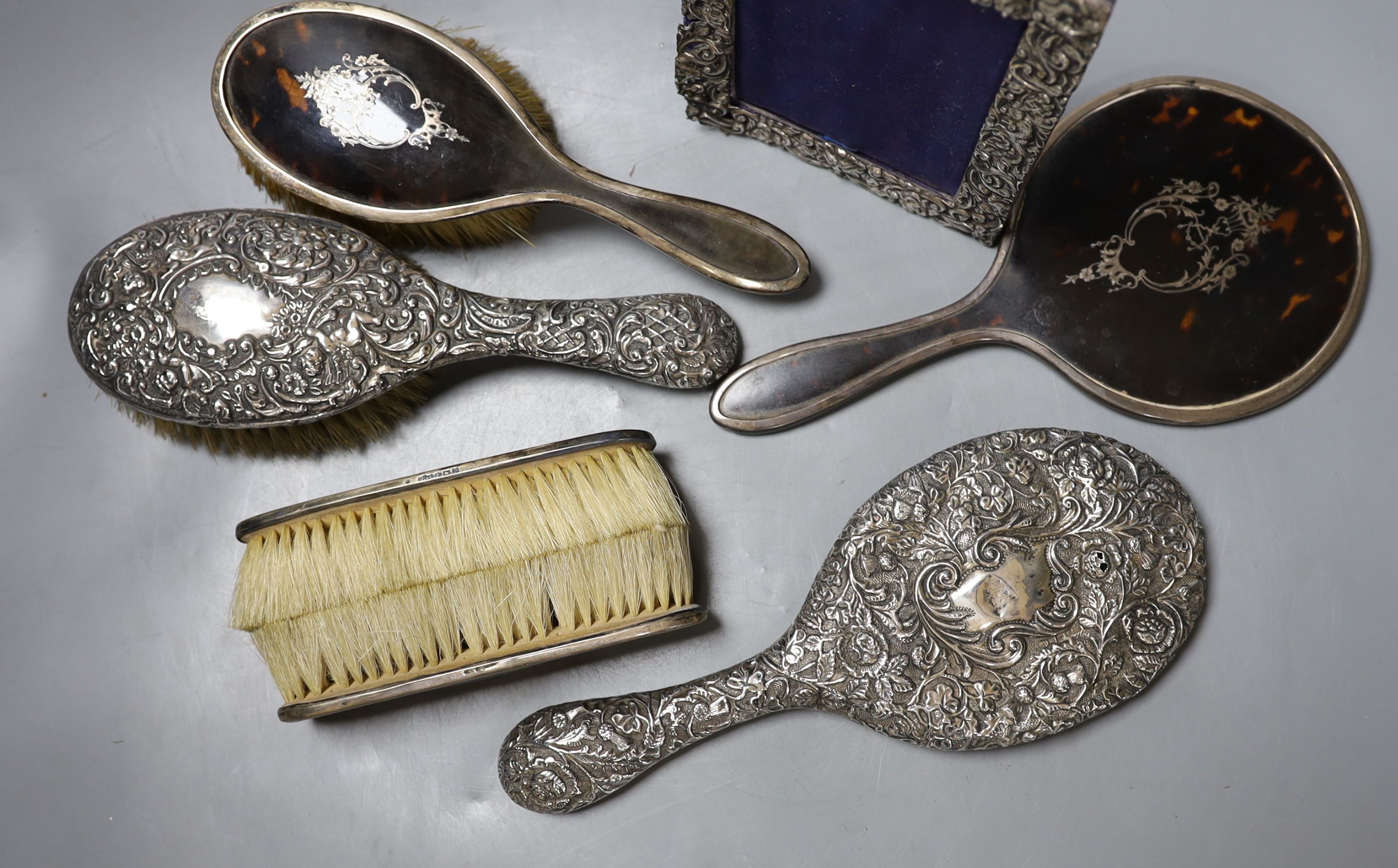 A George V silver and tortoiseshell mounted brush set and a tow similar embossed silver items(a.f.) and a silver mounted photograph frame.